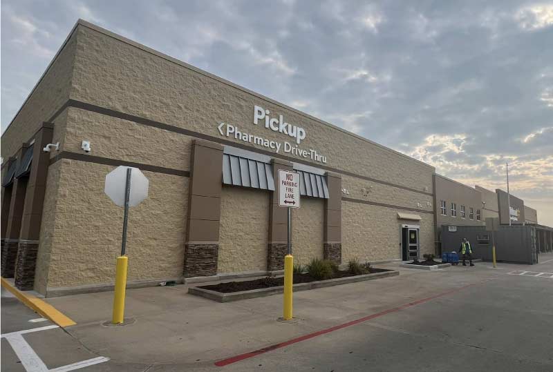 A professional commercial exterior paint job for a large retail pharmacy and pickup building in Kansas City, featuring clean tan and brown masonry walls with gray awnings under a cloudy sky, by the best building painters in kansas city