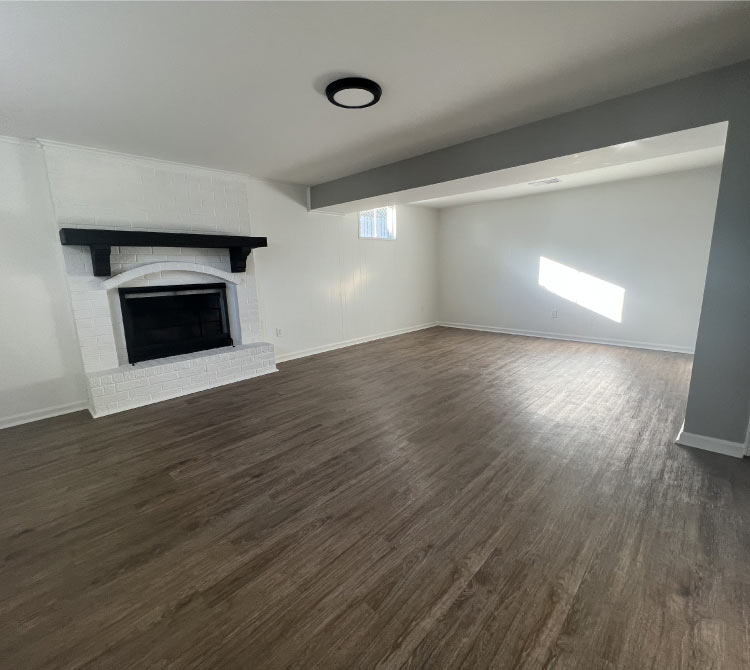 Interior house painting of a finished basement living area in Kansas City, featuring white walls, a brick fireplace, and new flooring