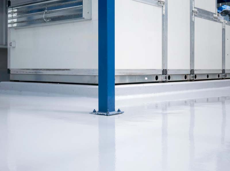 A pristine, light-colored commercial epoxy floor in an industrial facility, showing a seamless finish around structural supports and equipment.