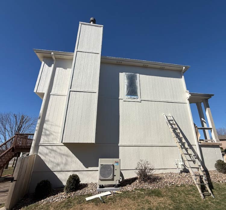 A freshly painted white two-story home in Kansas City featuring professional exterior restoration and stucco repair by Elite77 Painters. The image displays a tall chimney, clean siding, and a ladder positioned for high-quality exterior maintenance.  