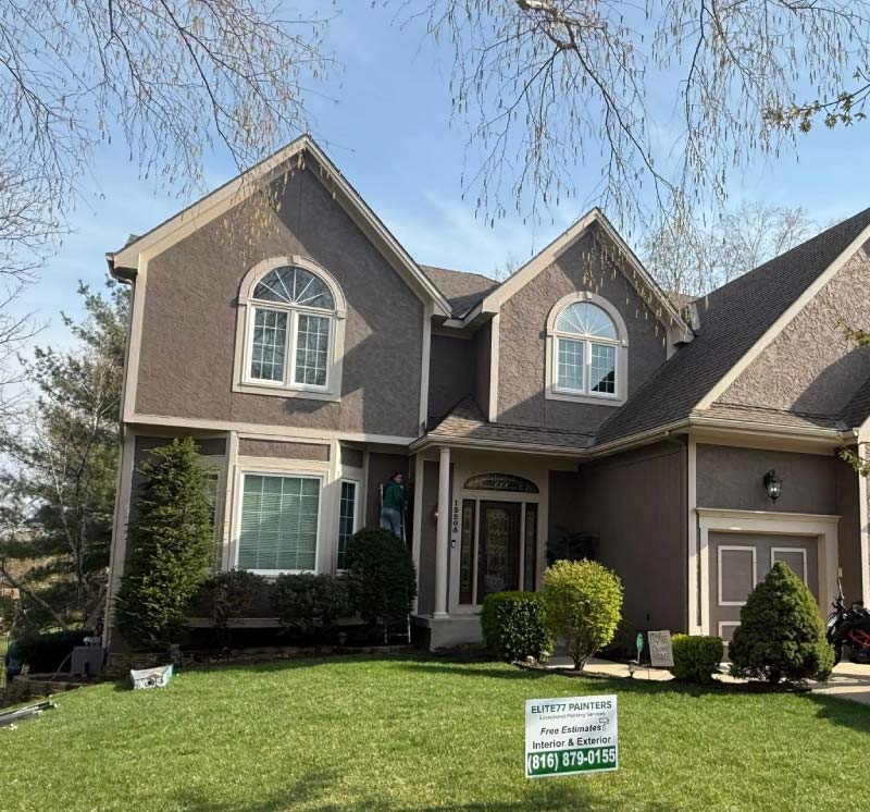 Two-story Kansas City home with freshly painted taupe stucco, board siding and cream trim, with an Elite77 Painters yard sign