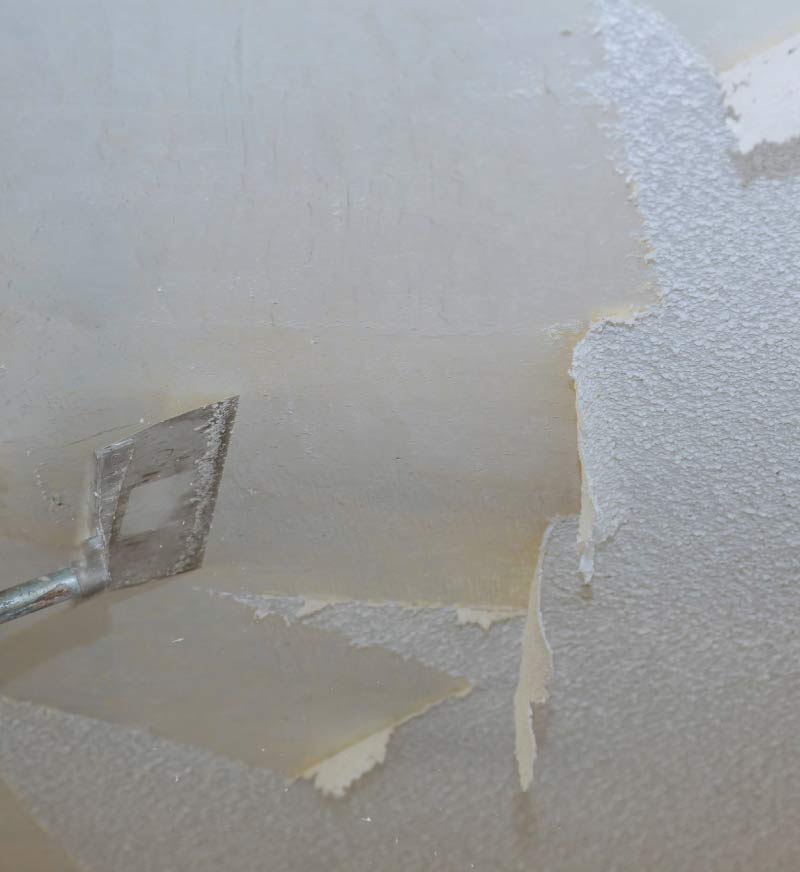 Close-up of a putty knife scraping popcorn texture off a ceiling during professional popcorn ceiling removal