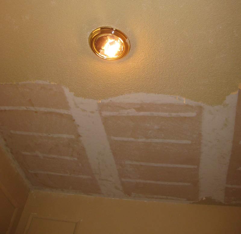 Popcorn ceiling removal in progress showing a skim-coated, smoothed section next to remaining textured ceiling around a light fixture